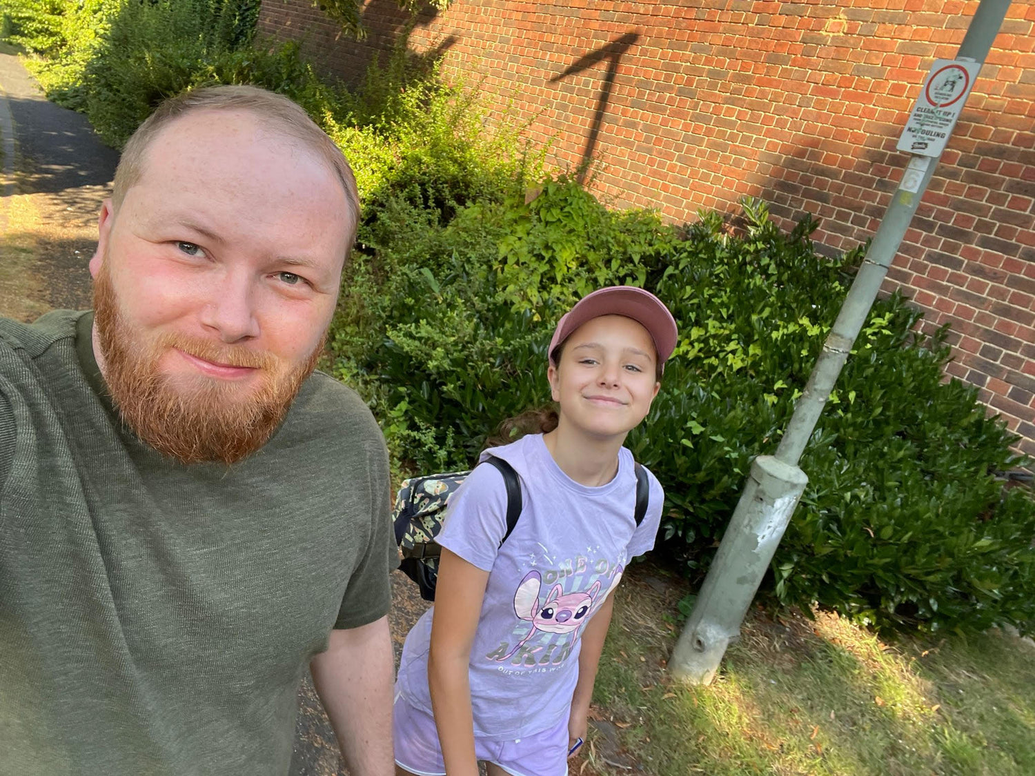 Man and child standing outdoors next to a brick wall and greenery