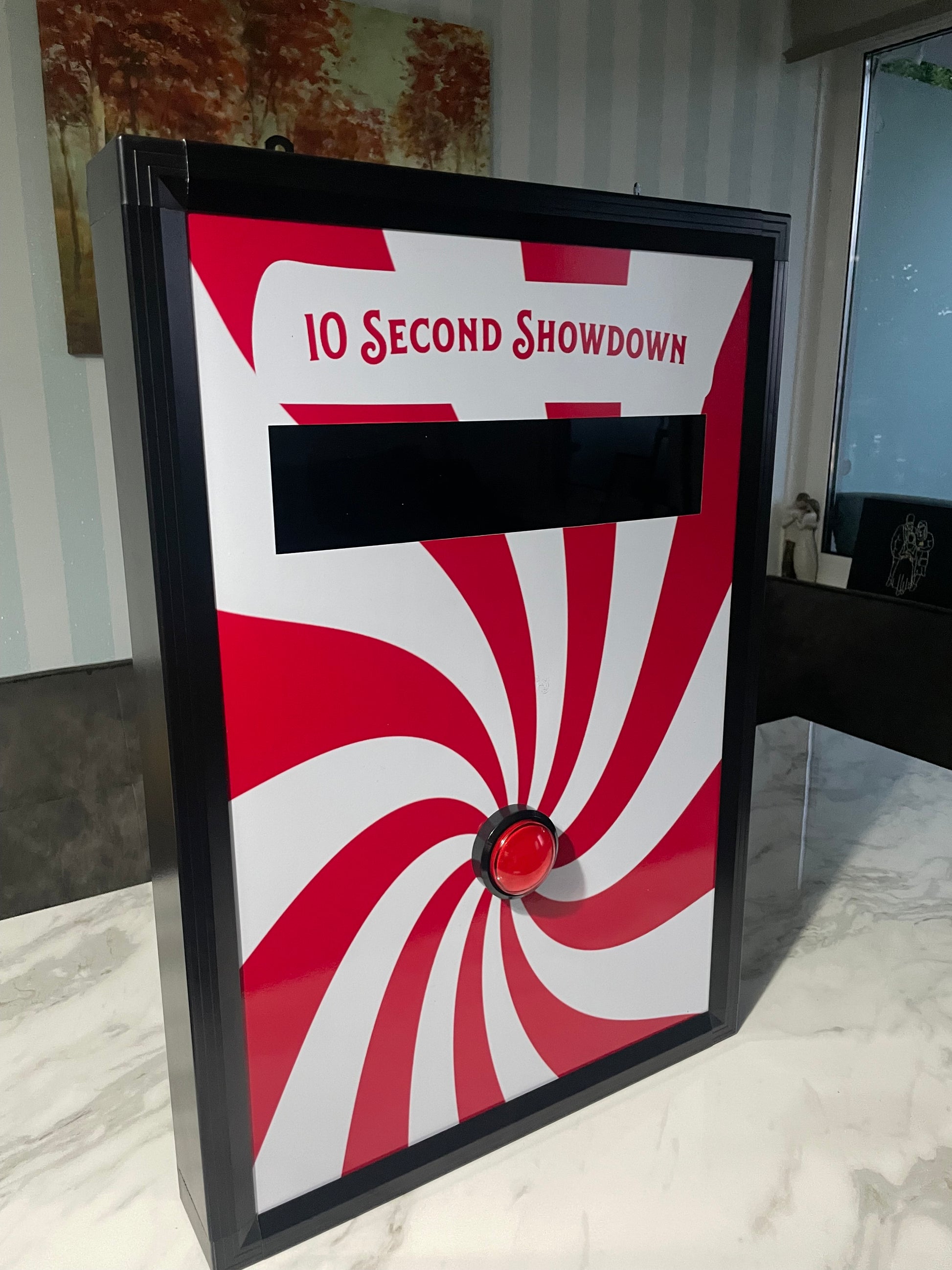 10 Second challenge - Red and white spiral design with a black rectangle and red button on a black border, placed on a surface.