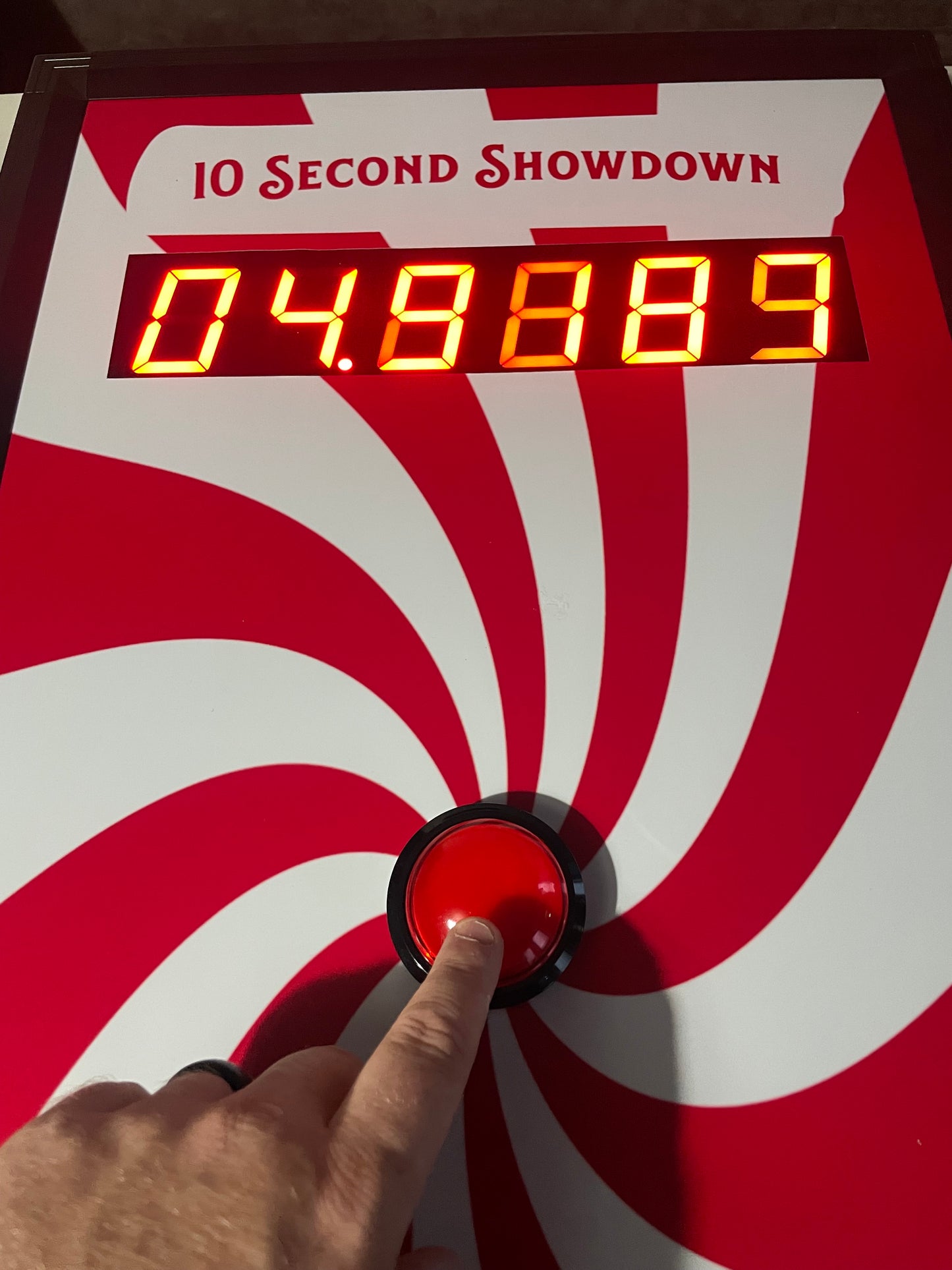 10 Second challenge - Hand pressing a red button on a countdown device with a red and white spiral design.