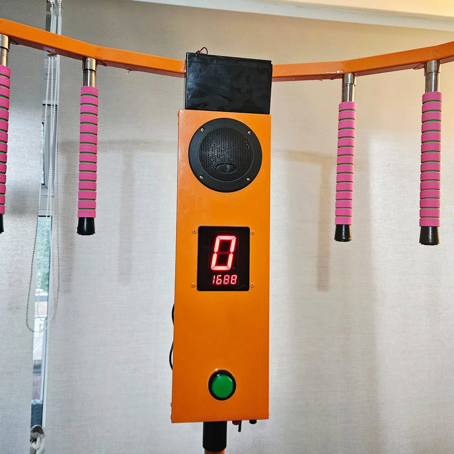 Orange control panel with digital display and speaker on a wall with pink and black handles.