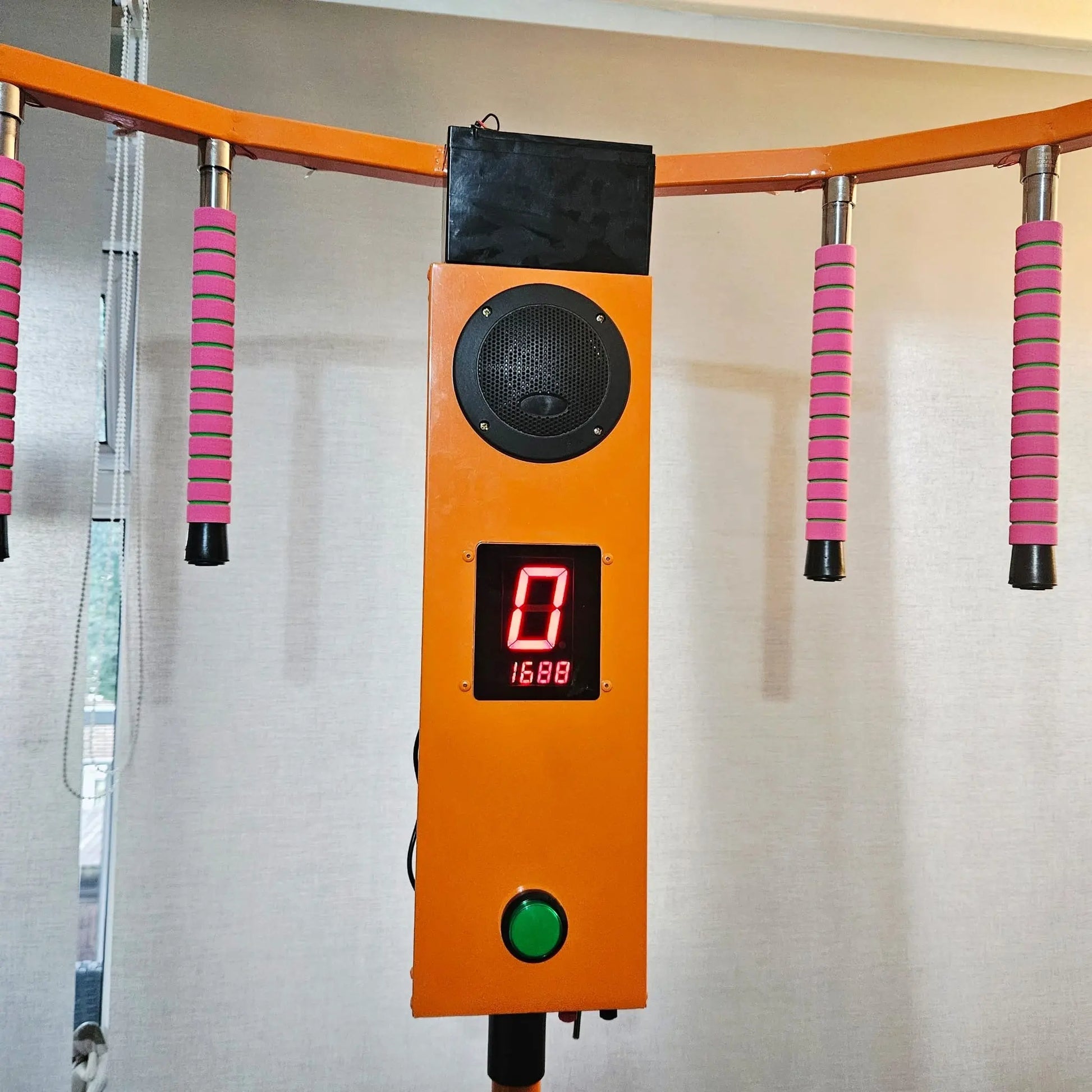 Orange control panel with digital display and speaker on a wall with pink and black handles.