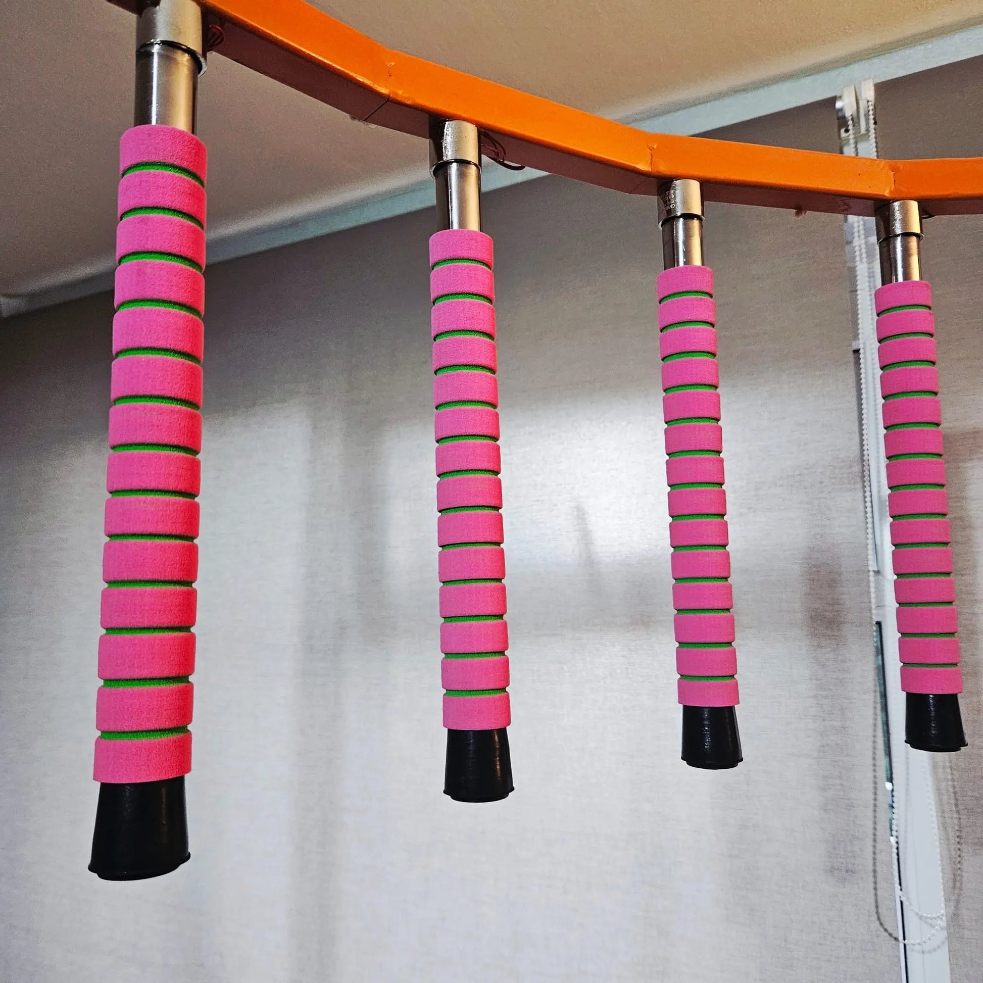 Pink and green resistance bars attached to a wooden bar on a plain background
