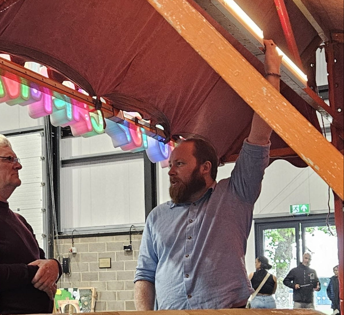 Two men standing under a carnival-style canopy with colorful lights and a 'Big Top Carnival Co.' sign.