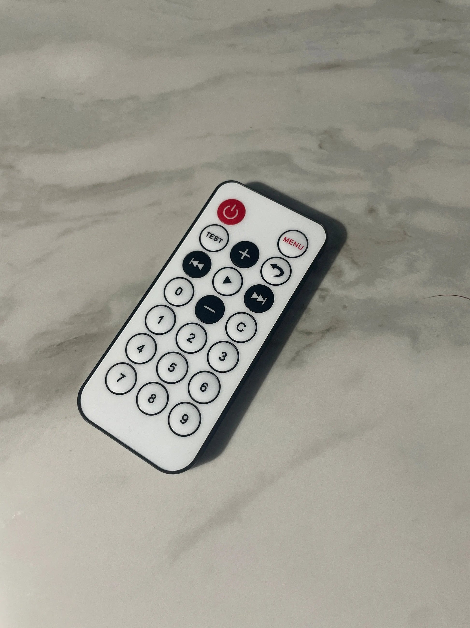 Black remote control with white buttons on a marble surface