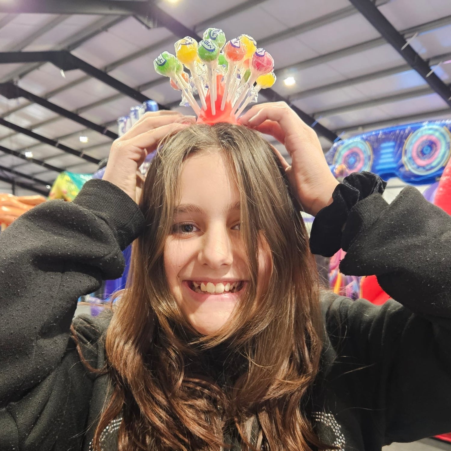 Person wearing a colorful crown made of lollipops in an indoor playground setting.